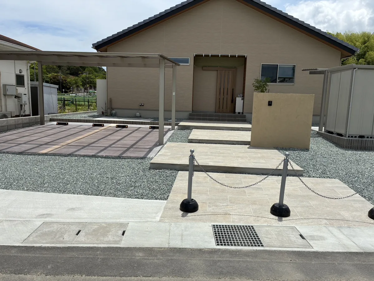 平屋住宅の外構全景。2台用カーポートとタイル貼り駐車スペース、物置、砂利敷きのオープン外構